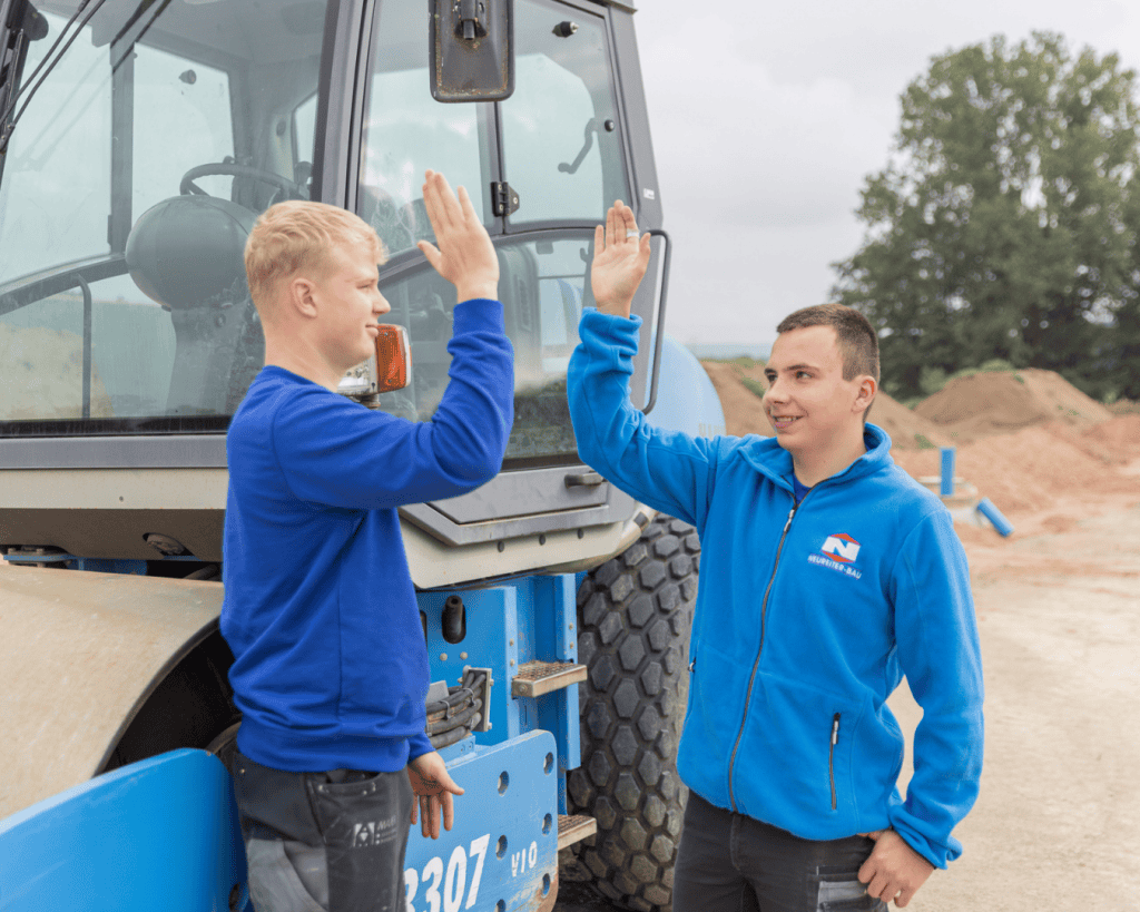Zwei Auszubildende eines Bauunternehmens an einer Baumaschine während der Ausbildung im Handwerk